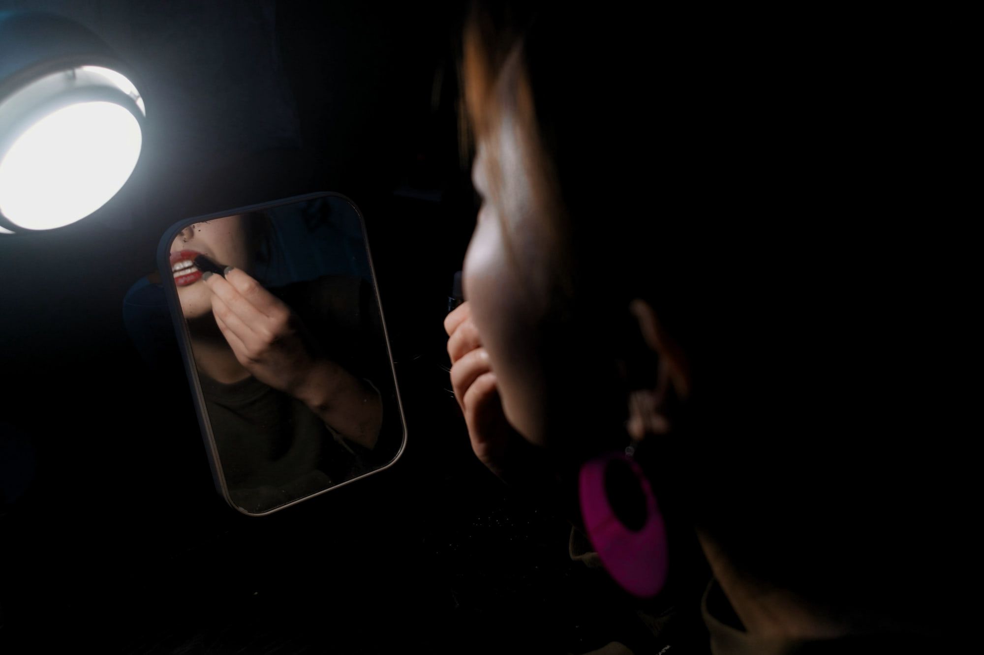 A dark room lit by a single lamp, a woman reflected in a small mirror.