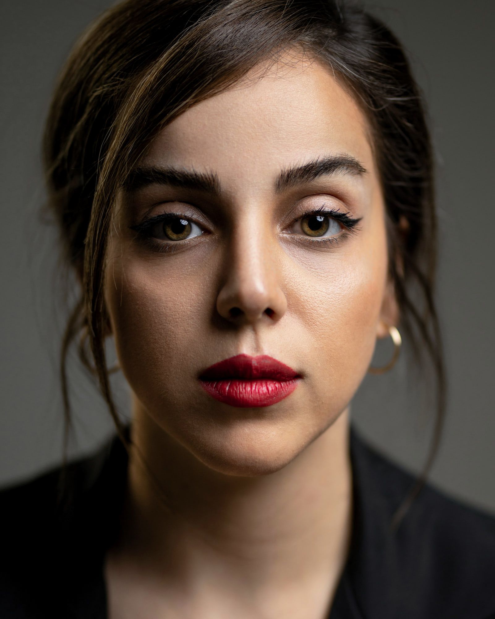 A woman in a dark jacket looks straight at the camera, her lips a clean red.